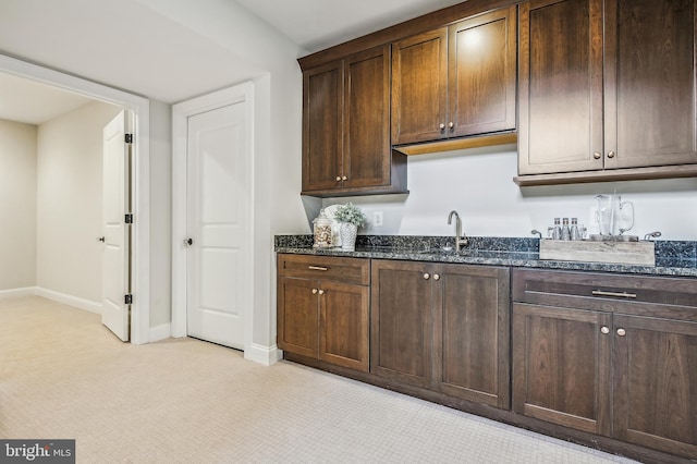 kitchen with sink, dark stone counters, light carpet, and dark brown cabinetry