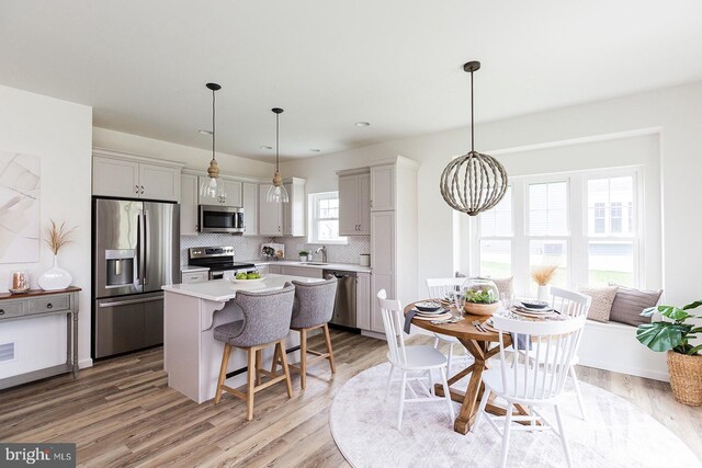 kitchen featuring hanging light fixtures, appliances with stainless steel finishes, light hardwood / wood-style flooring, backsplash, and an inviting chandelier