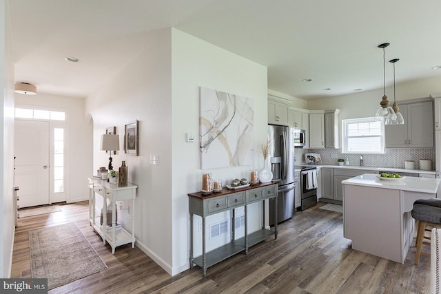 kitchen featuring decorative light fixtures, dark wood-type flooring, stainless steel appliances, backsplash, and a kitchen breakfast bar