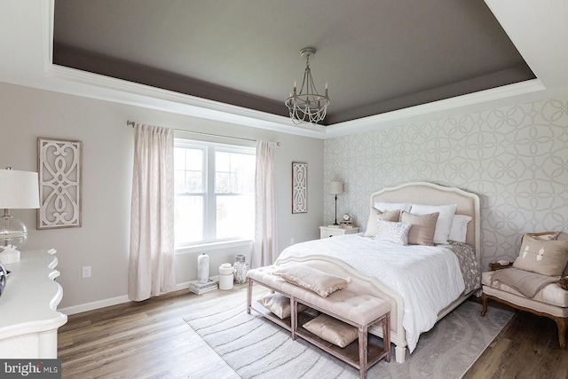 bedroom with a raised ceiling, hardwood / wood-style flooring, and a chandelier