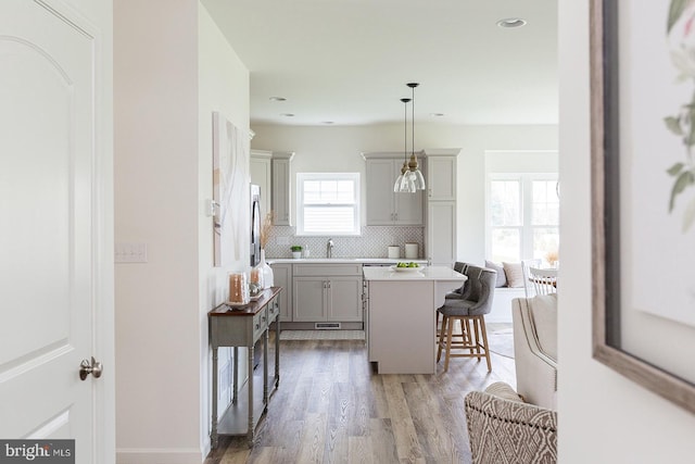 kitchen with tasteful backsplash, gray cabinets, light wood-type flooring, pendant lighting, and a kitchen breakfast bar