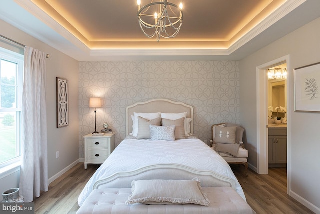 bedroom featuring an inviting chandelier, ensuite bath, dark hardwood / wood-style floors, and a raised ceiling