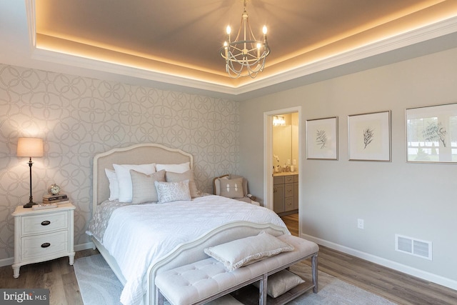 bedroom featuring an inviting chandelier, connected bathroom, dark wood-type flooring, and a tray ceiling