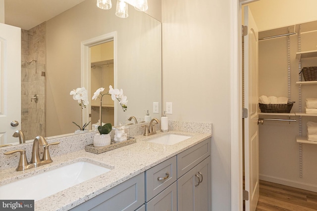 bathroom with large vanity, dual sinks, a tile shower, and hardwood / wood-style flooring