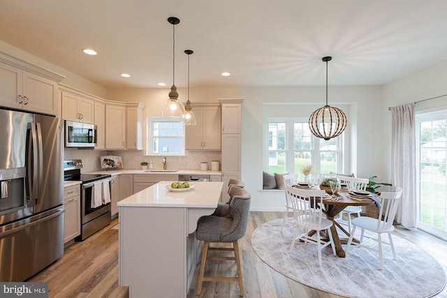 kitchen featuring a kitchen island, appliances with stainless steel finishes, tasteful backsplash, decorative light fixtures, and light wood-type flooring