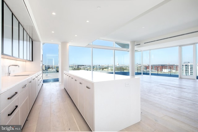 kitchen featuring white cabinets, light hardwood / wood-style floors, a kitchen island, and sink