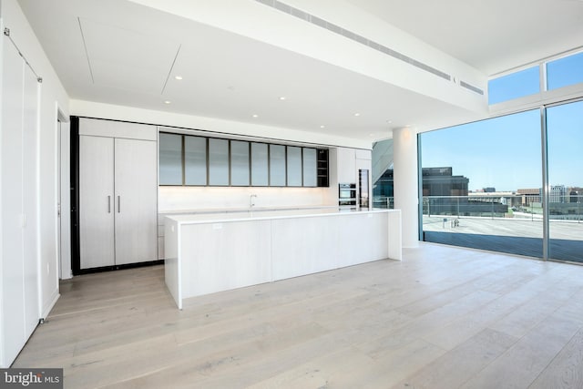 kitchen with floor to ceiling windows, a center island with sink, tasteful backsplash, and light hardwood / wood-style floors