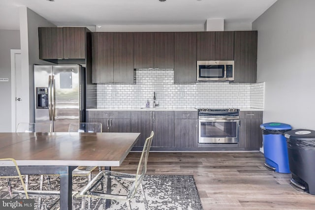 kitchen with tasteful backsplash, dark brown cabinets, dark wood-type flooring, appliances with stainless steel finishes, and sink