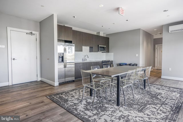 kitchen with stainless steel fridge, a wall mounted air conditioner, dark hardwood / wood-style flooring, backsplash, and dark brown cabinetry