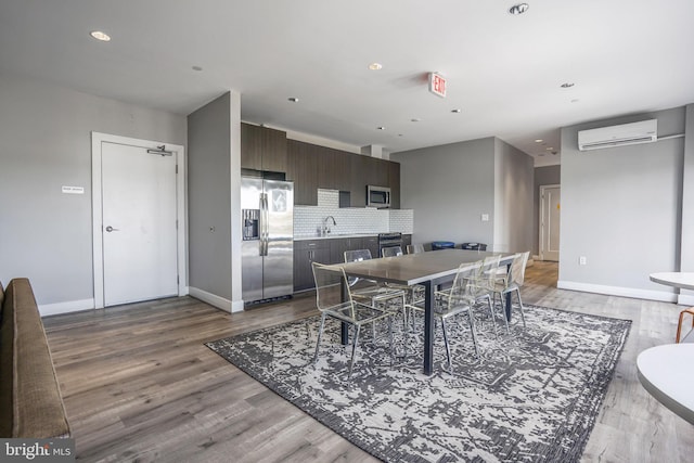 dining space with a wall unit AC, sink, and light wood-type flooring