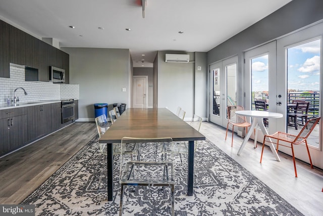 dining space featuring a wall mounted AC, light hardwood / wood-style floors, french doors, and sink