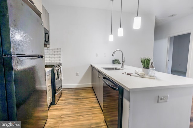 kitchen featuring appliances with stainless steel finishes, pendant lighting, backsplash, light hardwood / wood-style floors, and sink