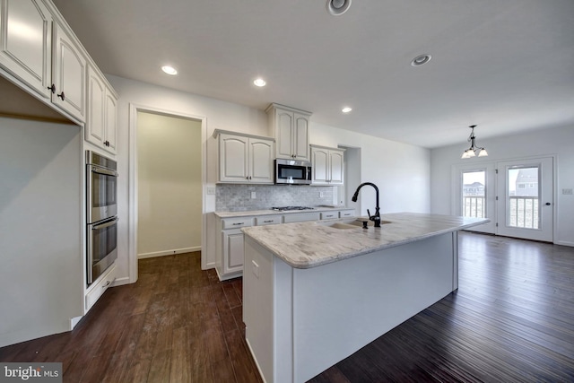 kitchen with stainless steel appliances, white cabinetry, dark hardwood / wood-style flooring, a kitchen island with sink, and sink