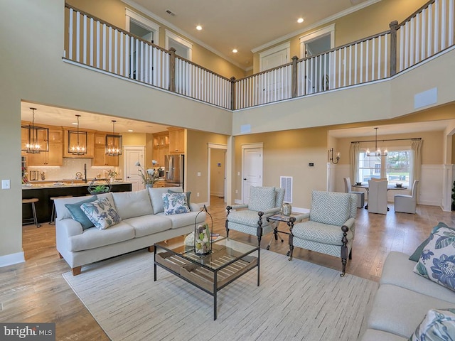 living room with an inviting chandelier, sink, light wood-type flooring, and a towering ceiling