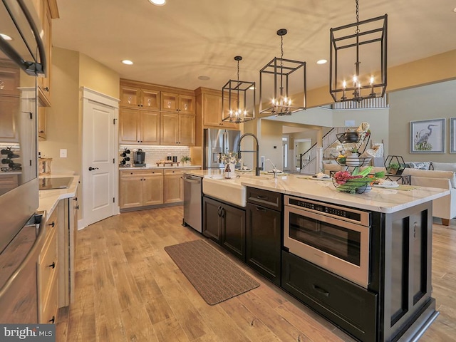 kitchen with an island with sink, pendant lighting, light hardwood / wood-style floors, appliances with stainless steel finishes, and backsplash