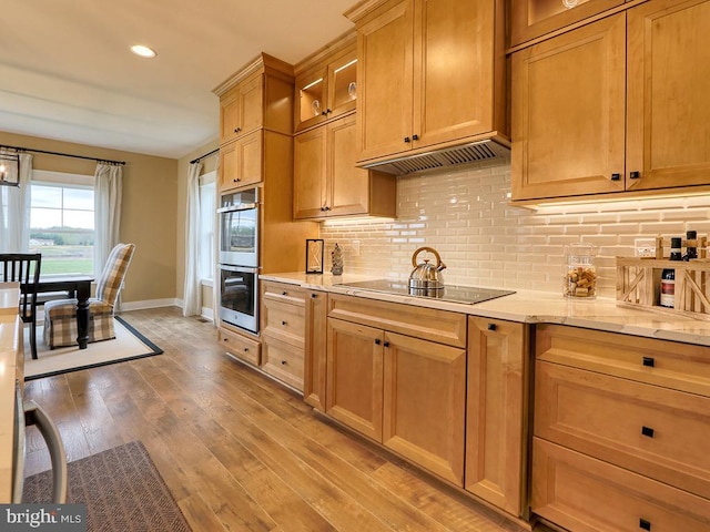 kitchen featuring light stone counters, black electric stovetop, light wood-type flooring, double oven, and backsplash