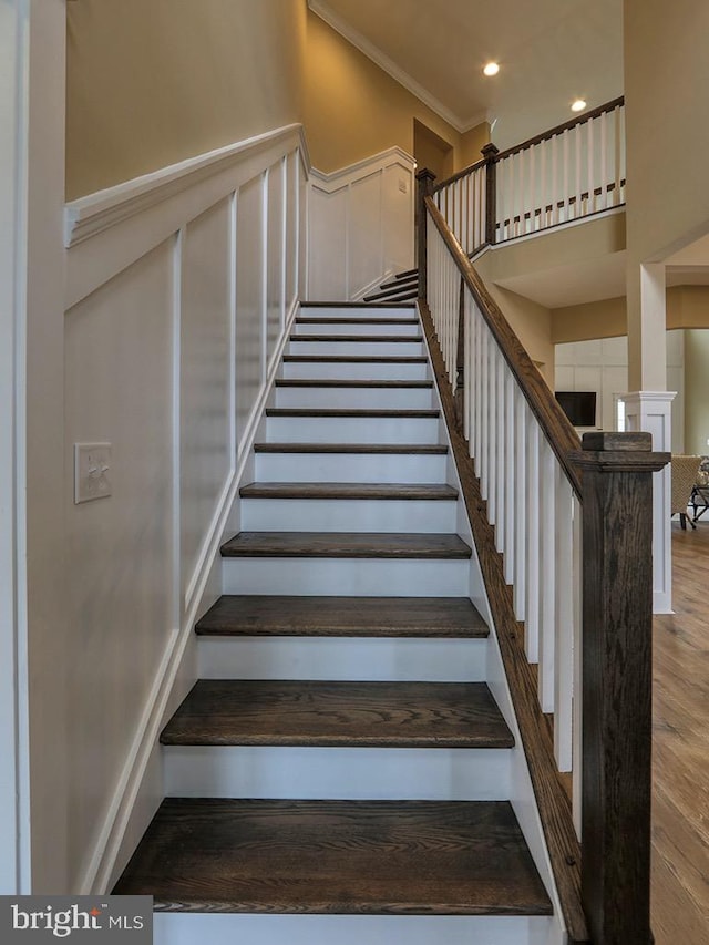 stairway with dark hardwood / wood-style flooring, crown molding, and a towering ceiling