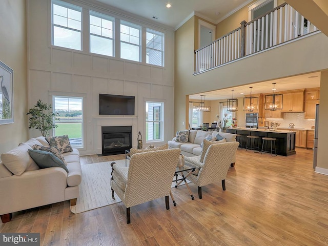 living room featuring light hardwood / wood-style flooring, crown molding, an inviting chandelier, and a high ceiling