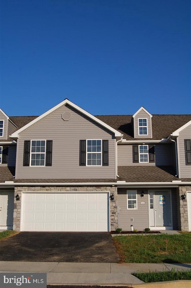 townhome / multi-family property featuring a garage, stone siding, roof with shingles, and driveway