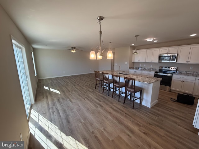 kitchen featuring light stone counters, stainless steel appliances, white cabinetry, an island with sink, and wood finished floors