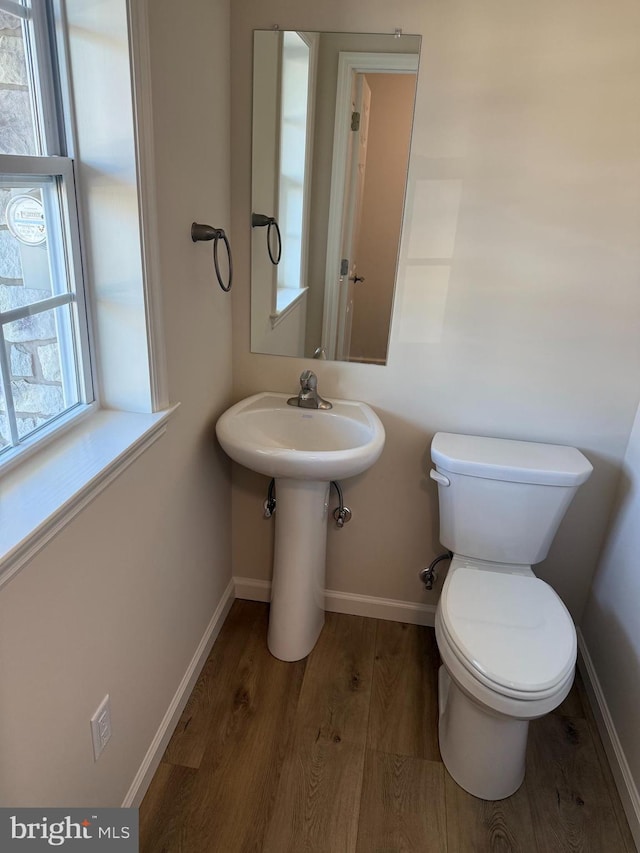 half bath with baseboards, toilet, and wood finished floors