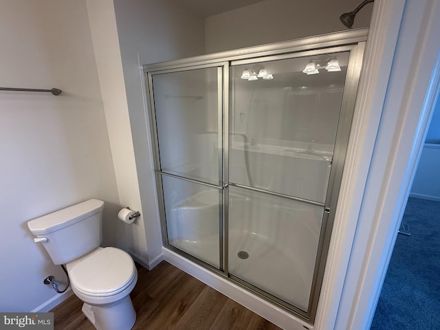 bathroom featuring toilet, a shower stall, baseboards, and wood finished floors