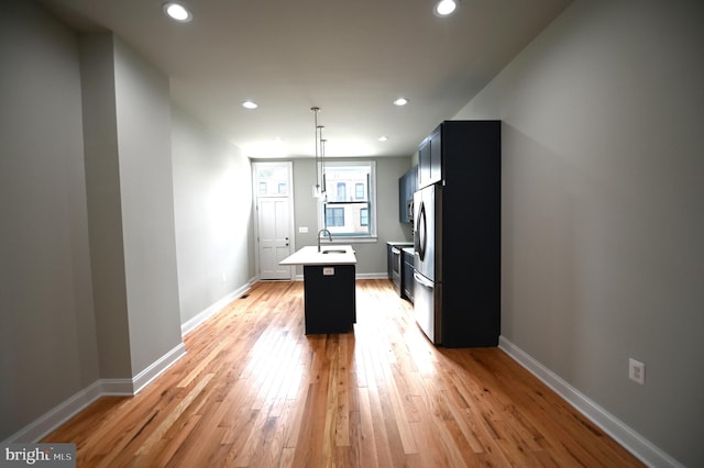 kitchen featuring stainless steel fridge, a center island with sink, and light wood-type flooring