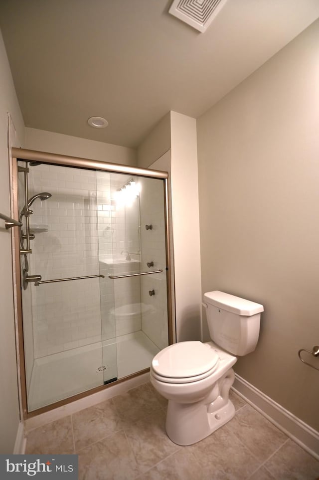 bathroom featuring toilet, a shower with shower door, and tile flooring