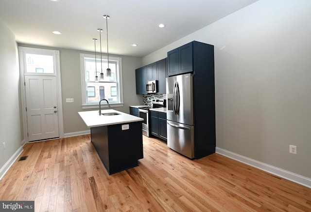 kitchen featuring decorative light fixtures, appliances with stainless steel finishes, sink, an island with sink, and light wood-type flooring