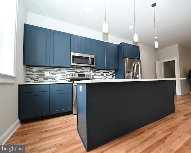 kitchen featuring stainless steel appliances, decorative light fixtures, blue cabinets, backsplash, and light wood-type flooring