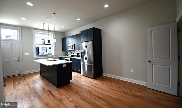 kitchen featuring an island with sink, decorative light fixtures, appliances with stainless steel finishes, and light wood-type flooring