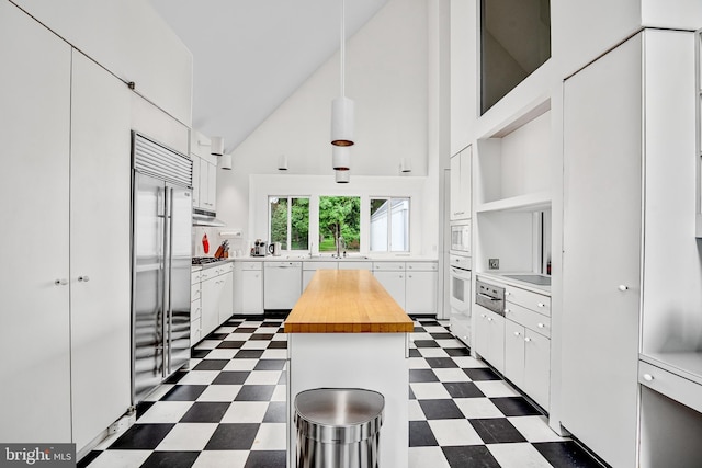 kitchen featuring built in appliances, high vaulted ceiling, white cabinets, a center island, and butcher block countertops