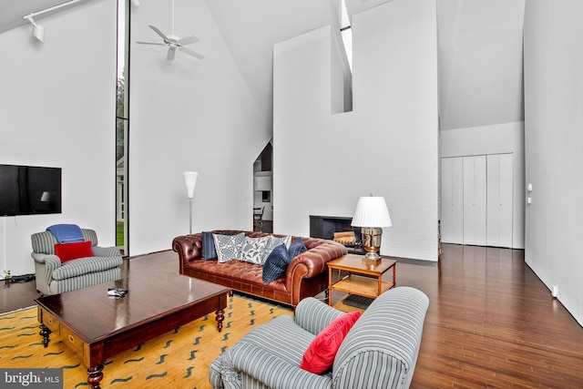 living room with a large fireplace, high vaulted ceiling, ceiling fan, and dark wood-type flooring