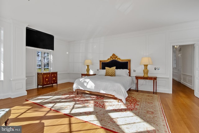 bedroom featuring wood-type flooring, crown molding, and decorative columns