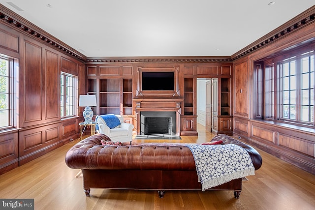 living room with crown molding, light hardwood / wood-style flooring, built in features, and wooden walls