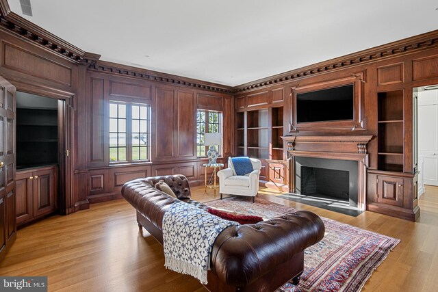 living room with built in shelves, light hardwood / wood-style floors, and crown molding