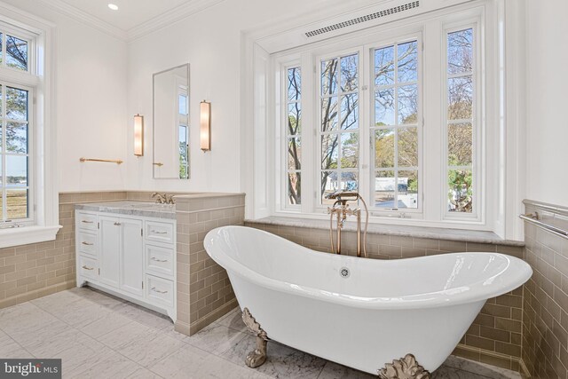 bathroom featuring a washtub, vanity, tile walls, and crown molding