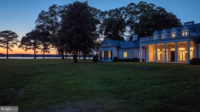 back house at dusk with a balcony, a yard, and french doors