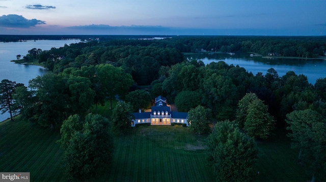aerial view at dusk with a wooded view and a water view