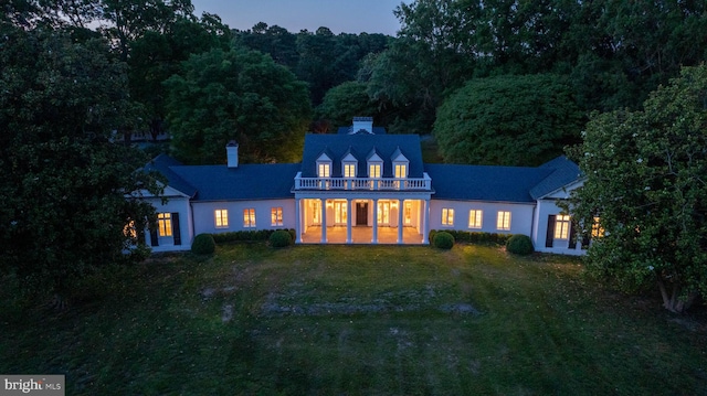 back house at dusk with a balcony and a lawn