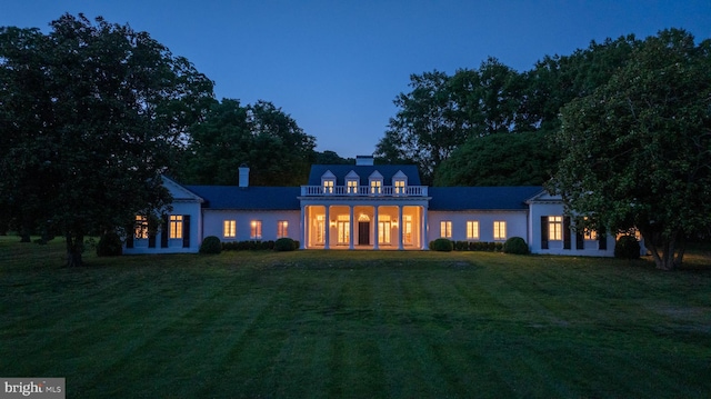 back of house at dusk with a lawn and a chimney