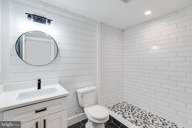 bathroom with a tile shower, tile flooring, toilet, and vanity