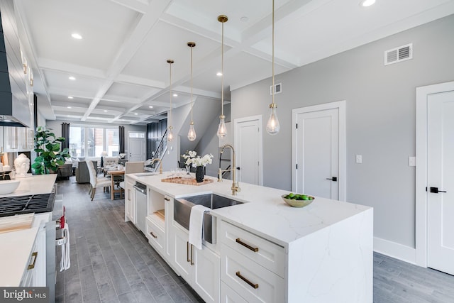 kitchen featuring an island with sink, beamed ceiling, dark wood-type flooring, light stone counters, and coffered ceiling