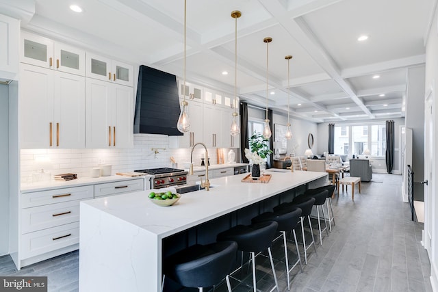 kitchen featuring backsplash, coffered ceiling, hardwood / wood-style flooring, and a kitchen island with sink