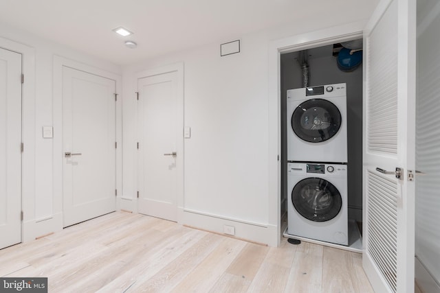 clothes washing area with stacked washer and clothes dryer and light wood-type flooring