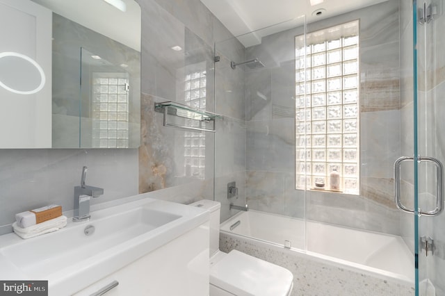 full bathroom with tile walls, combined bath / shower with glass door, toilet, and vanity with extensive cabinet space