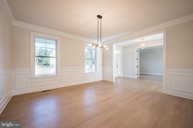 spare room with an inviting chandelier, ornamental molding, and light hardwood / wood-style floors