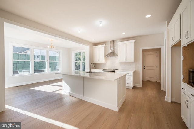 kitchen featuring white cabinetry, a center island with sink, light hardwood / wood-style flooring, wall chimney exhaust hood, and sink