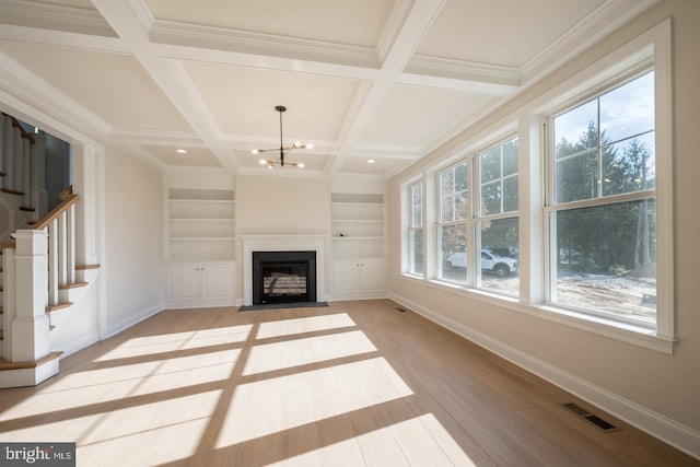 unfurnished living room featuring built in features, light hardwood / wood-style floors, coffered ceiling, a wealth of natural light, and an inviting chandelier