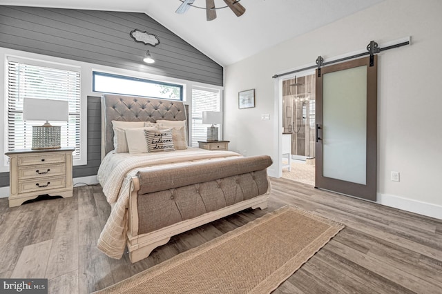 bedroom featuring a barn door, hardwood / wood-style floors, ceiling fan, and vaulted ceiling